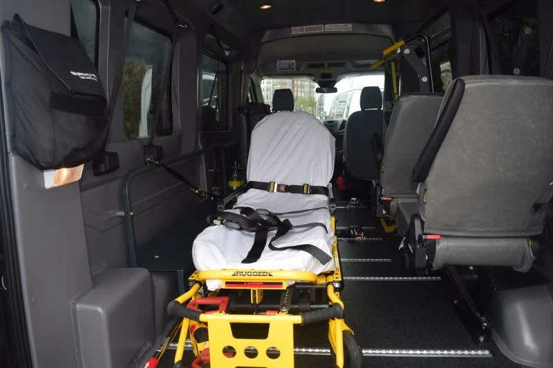 Stretcher strapped into the floor track of a medical transport van beside folding passenger seats