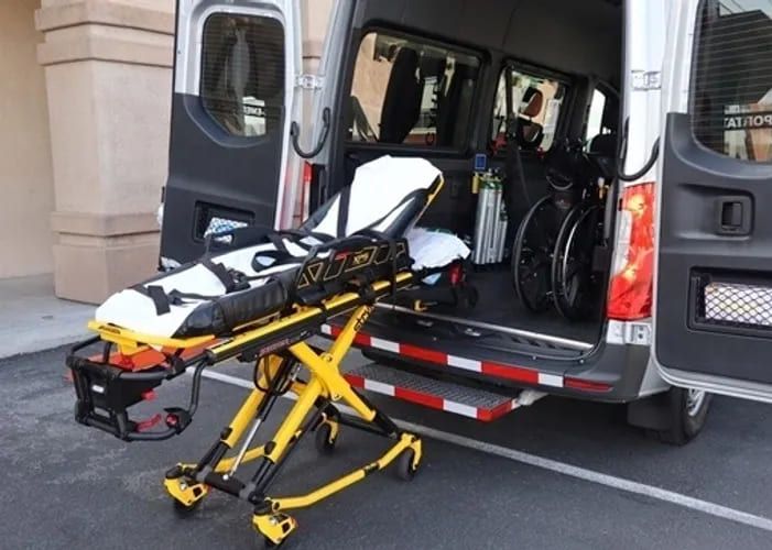 Stretcher raised at the rear of a transport van with a folded wheelchair and oxygen stored inside